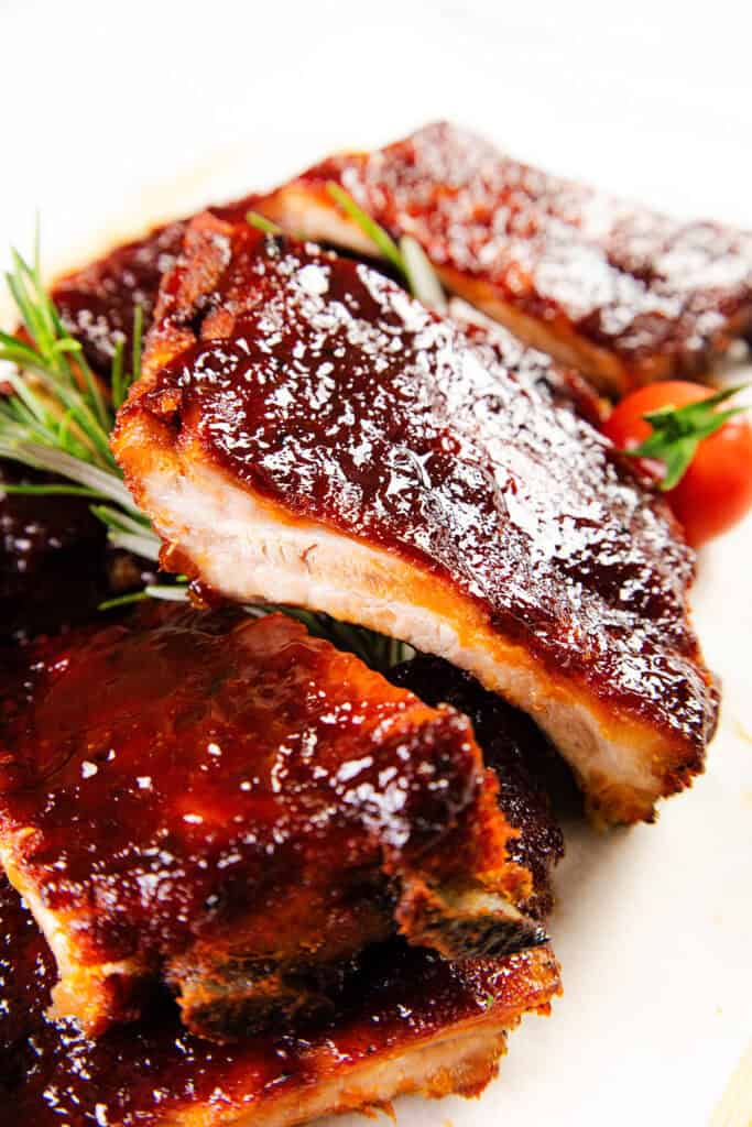 Close-up of grilled BBQ ribs with glossy caramelized BBQ glaze, single rib being pulled away to show tender fall-off-the-bone meat