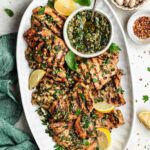 Perfectly grilled chicken thighs on a white plate with fresh herbs and lemon wedges, beautifully charred grill marks visible