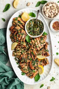 Perfectly grilled chicken thighs on a white plate with fresh herbs and lemon wedges, beautifully charred grill marks visible