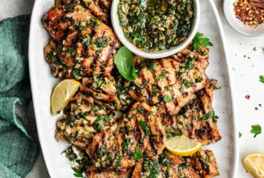 Grilled Chicken Thighs — The Juicy, Flavor-Packed Weeknight Grill Staple You'll Make on Repeat 27 Perfectly grilled chicken thighs on a white plate with fresh herbs and lemon wedges, beautifully charred grill marks visible
