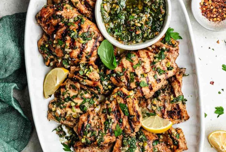 Perfectly grilled chicken thighs on a white plate with fresh herbs and lemon wedges, beautifully charred grill marks visible