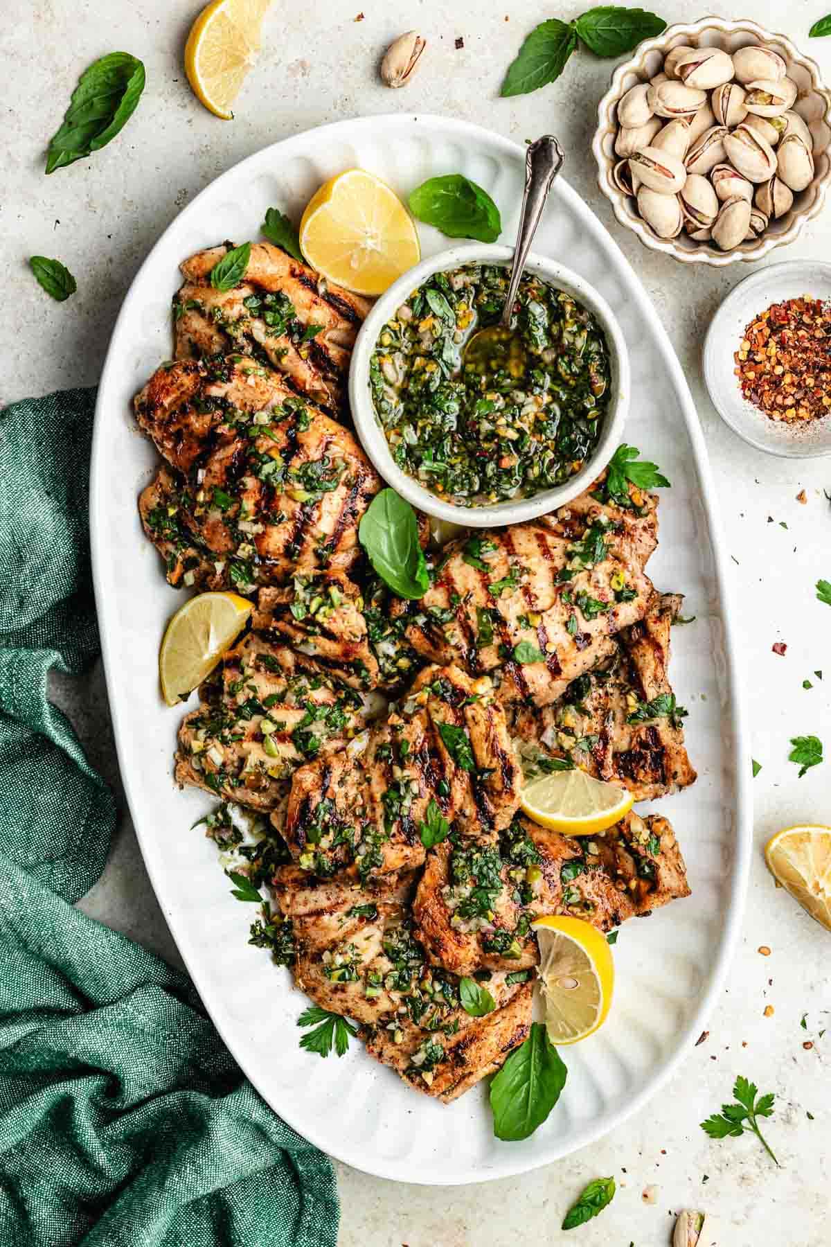 Perfectly grilled chicken thighs on a white plate with fresh herbs and lemon wedges, beautifully charred grill marks visible