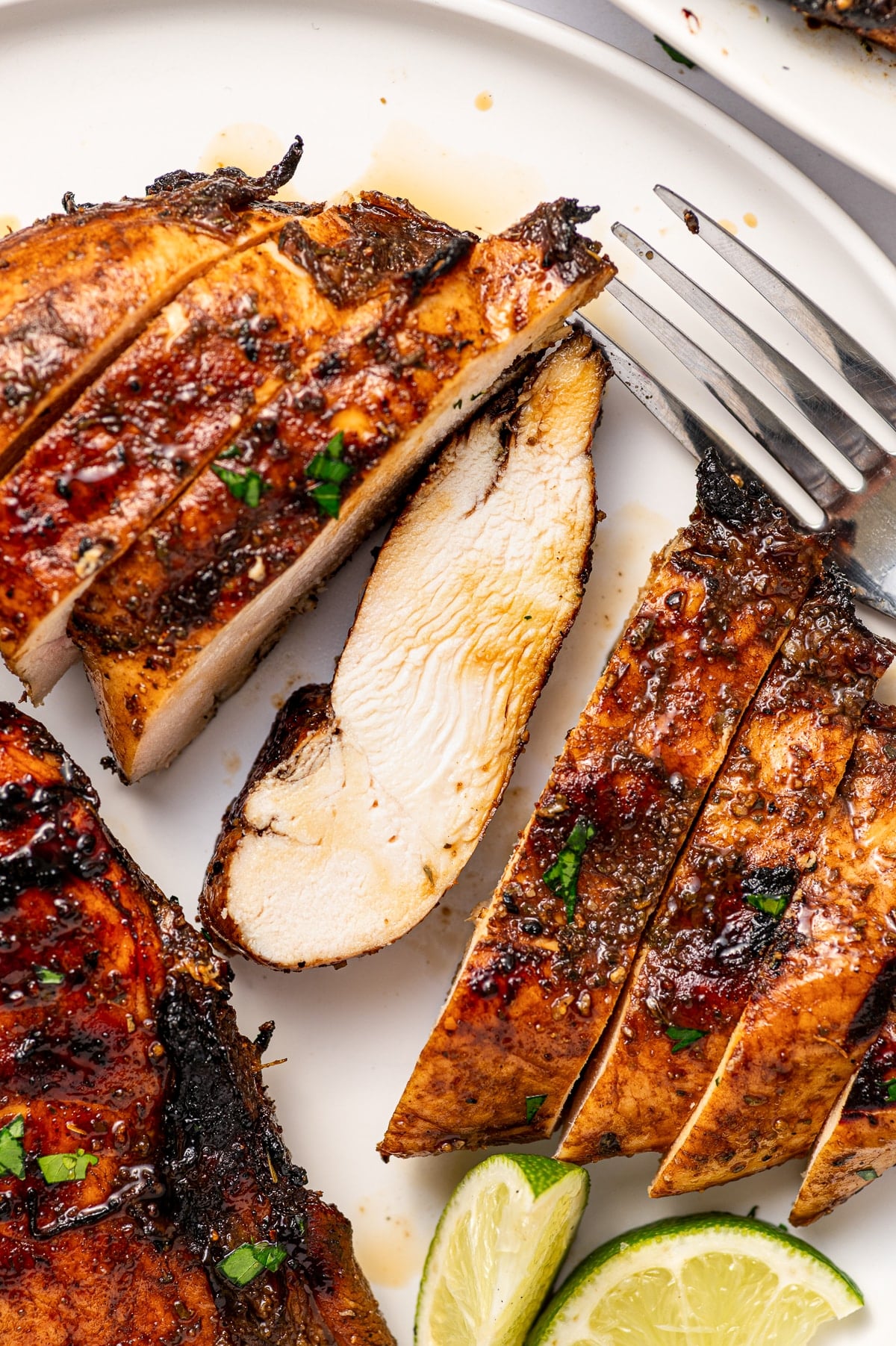 Close-up of a sliced grilled chicken thigh showing juicy interior with charred skin, served with roasted vegetables and a wedge of lemon on a wooden board