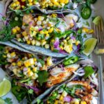 Grilled Fish Tacos with Corn Salsa plated beautifully on a wooden board with lime wedges, fresh cilantro, and charred corn salsa