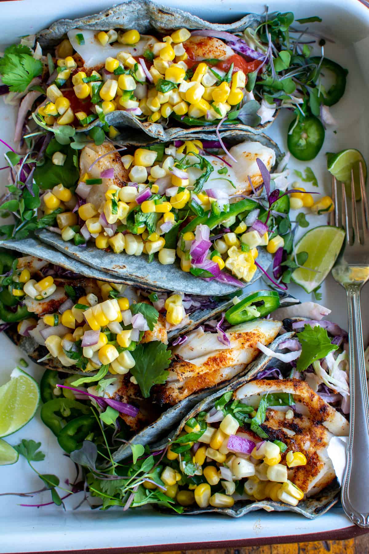 Grilled Fish Tacos with Corn Salsa plated beautifully on a wooden board with lime wedges, fresh cilantro, and charred corn salsa