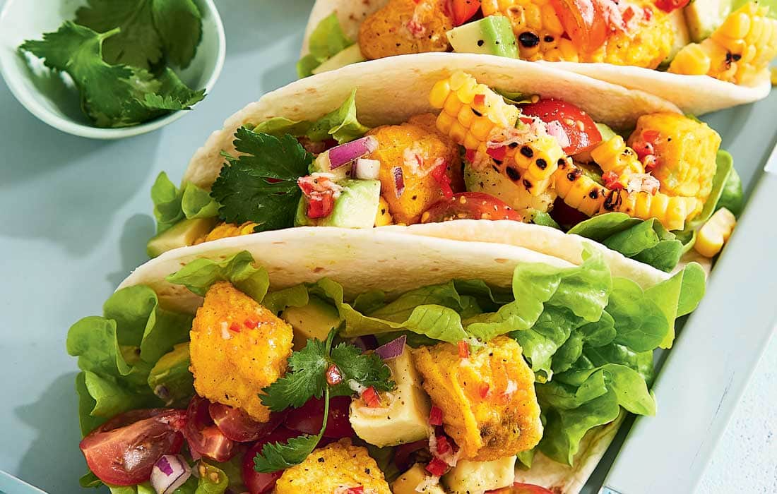 Close-up of a Grilled Fish Tacos with Corn Salsa in a charred corn tortilla, topped with avocado, corn salsa, and a squeeze of fresh lime