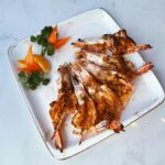 Grilled shrimp skewers beautifully plated on a white serving board with lemon wedges, fresh parsley, and a smoky char, shot overhead in warm natural light