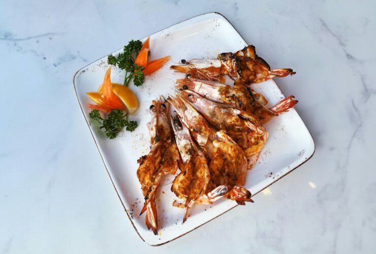 Grilled shrimp skewers beautifully plated on a white serving board with lemon wedges, fresh parsley, and a smoky char, shot overhead in warm natural light