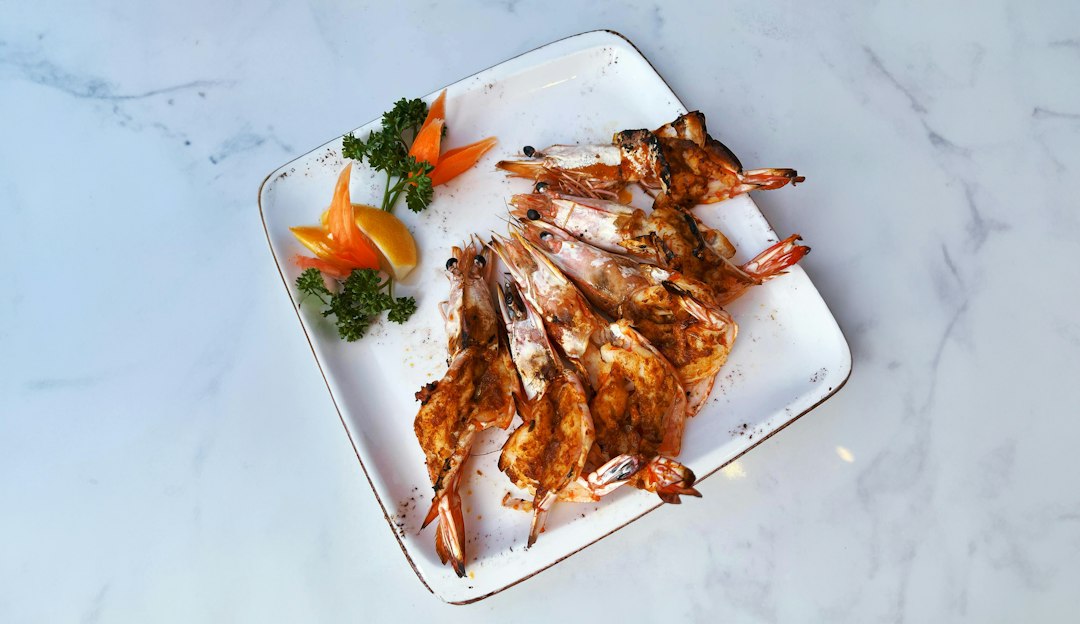 Grilled shrimp skewers beautifully plated on a white serving board with lemon wedges, fresh parsley, and a smoky char, shot overhead in warm natural light
