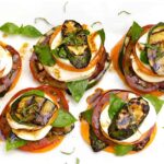 Grilled zucchini caprese stacks arranged on a white marble serving board, drizzled with balsamic glaze and garnished with fresh basil leaves