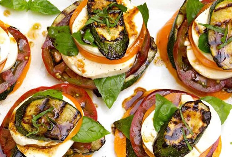 Grilled zucchini caprese stacks arranged on a white marble serving board, drizzled with balsamic glaze and garnished with fresh basil leaves