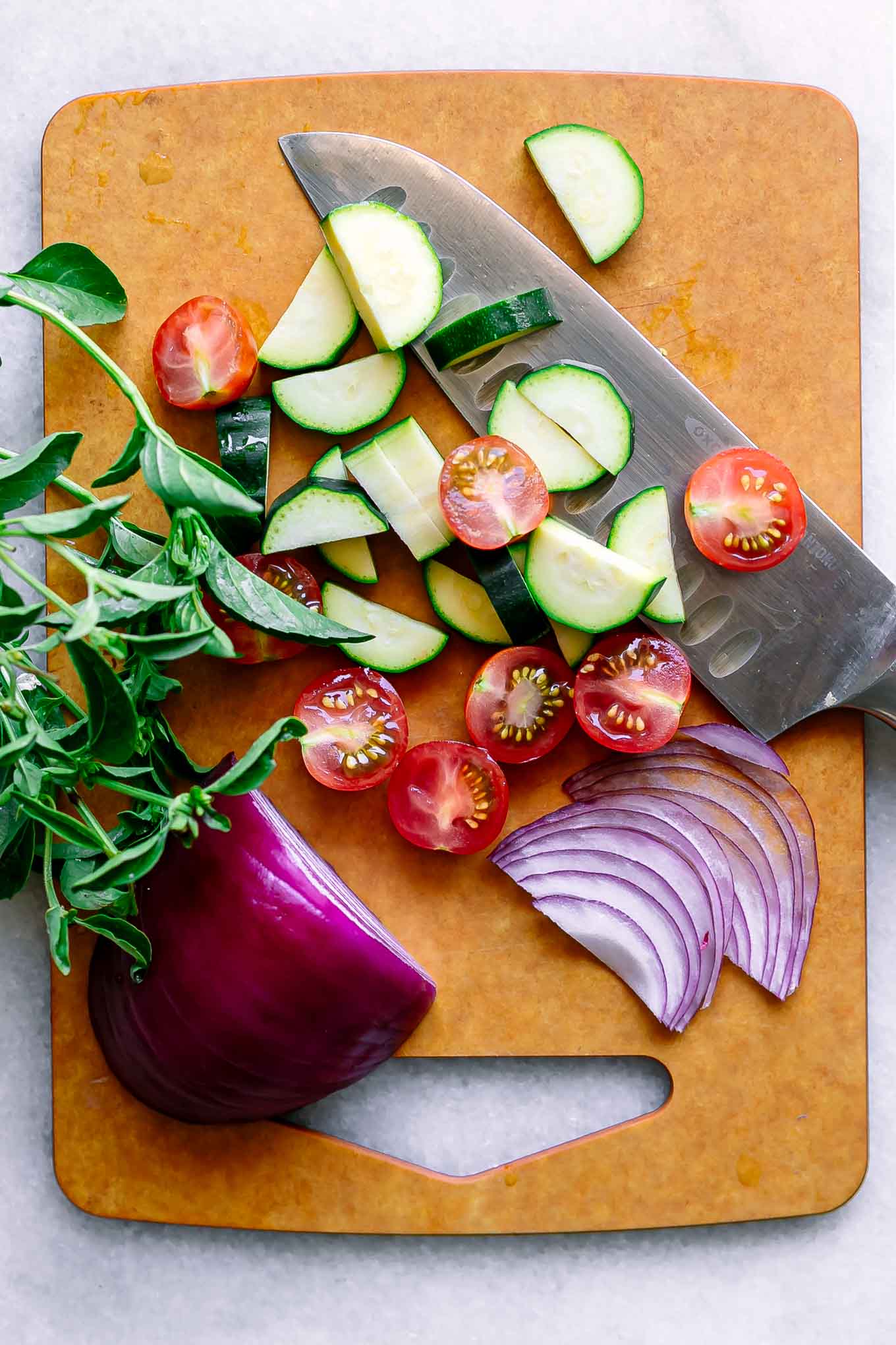 Sliced zucchini rounds, fresh mozzarella, ripe tomatoes, fresh basil, and small bowls of balsamic glaze and olive oil arranged on a wooden cutting board