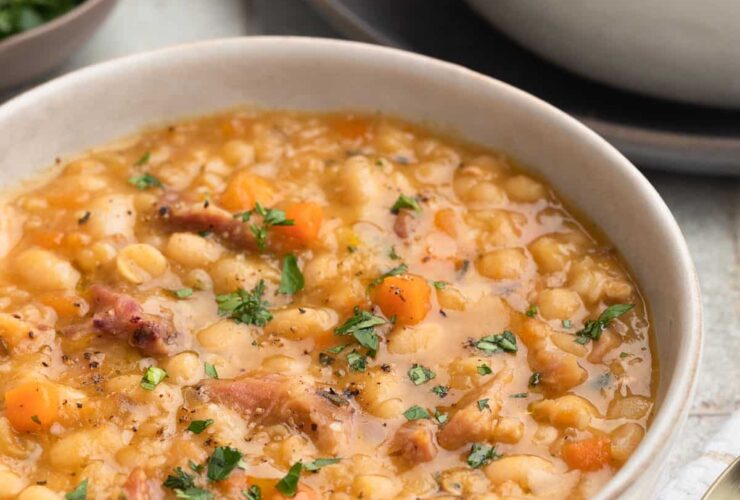 A rustic bowl of ham and bean soup with creamy white beans, tender chunks of ham, and fresh parsley garnish, photographed overhead on a wooden table