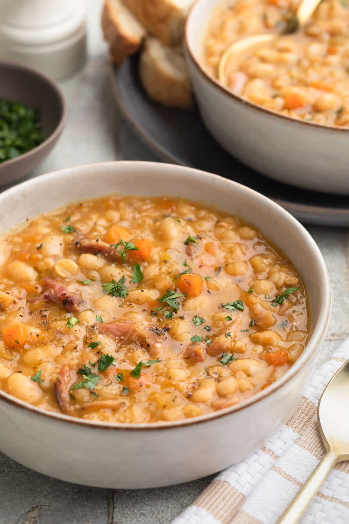 A rustic bowl of ham and bean soup with creamy white beans, tender chunks of ham, and fresh parsley garnish, photographed overhead on a wooden table