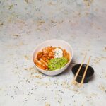 Hawaiian poke bowl with sushi-grade ahi tuna, steamed rice, edamame, cucumber, avocado, and sesame seeds in a white ceramic bowl, overhead shot, bright natural light