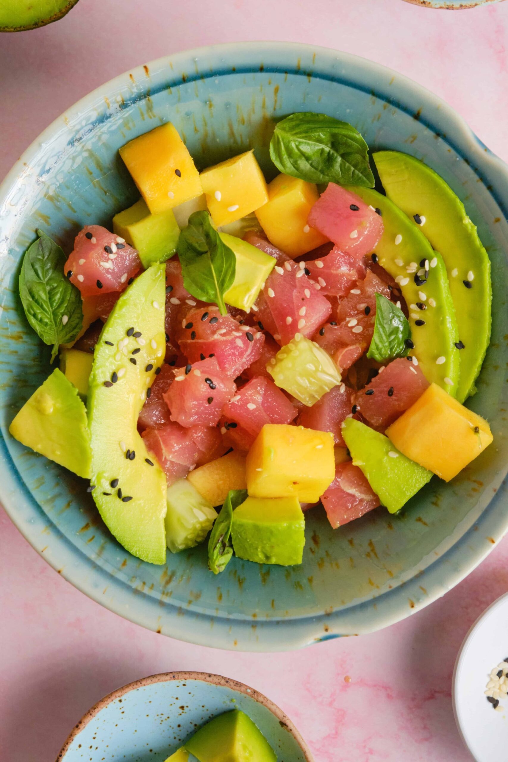 Poke bowl ingredients laid out flat — cubed ahi tuna, diced cucumber, sliced avocado, edamame, soy sauce, sesame oil, sriracha, rice, and sesame seeds on a marble surface, natural overhead lighting