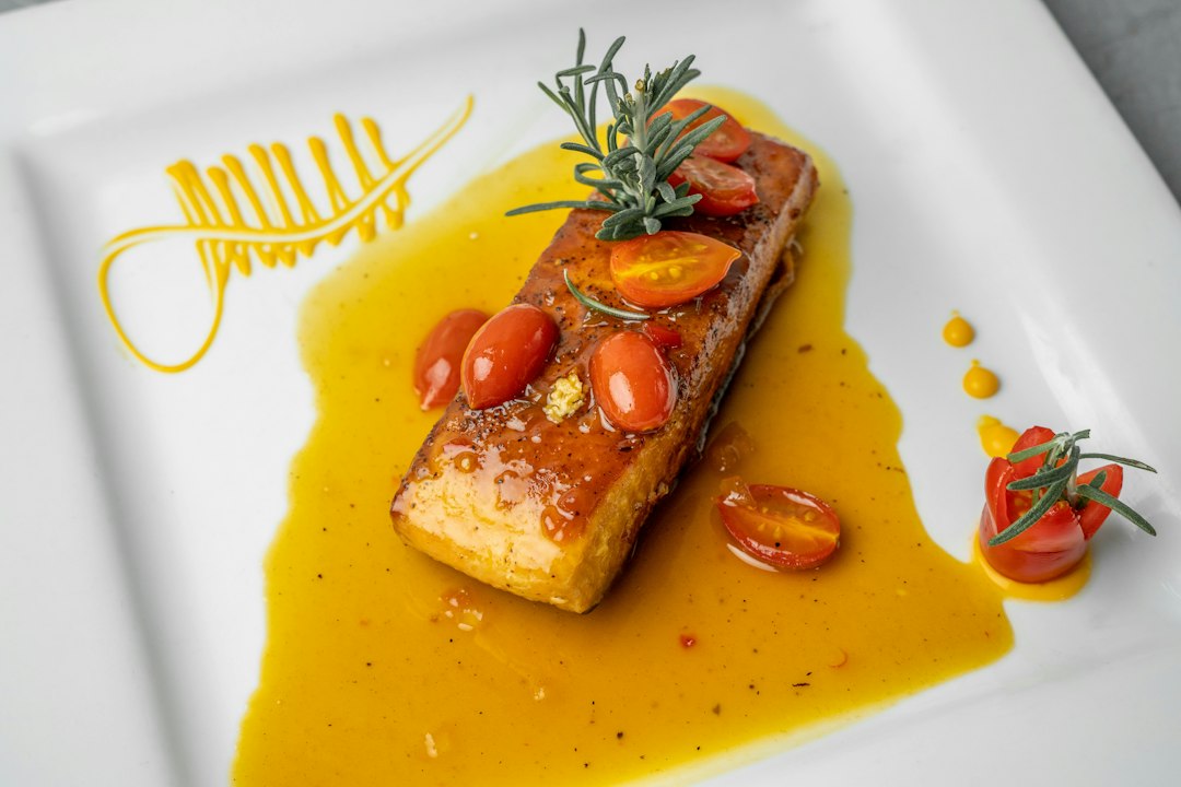 Herb-crusted salmon fillet with golden herb crust served on a white platter surrounded by roasted summer vegetables including zucchini, cherry tomatoes, and bell peppers, garnished with fresh basil and lemon wedges
