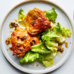 Hot Honey Chicken plated on a white ceramic dish with a glossy sweet-heat glaze, garnished with fresh thyme and chili flakes, served alongside roasted vegetables