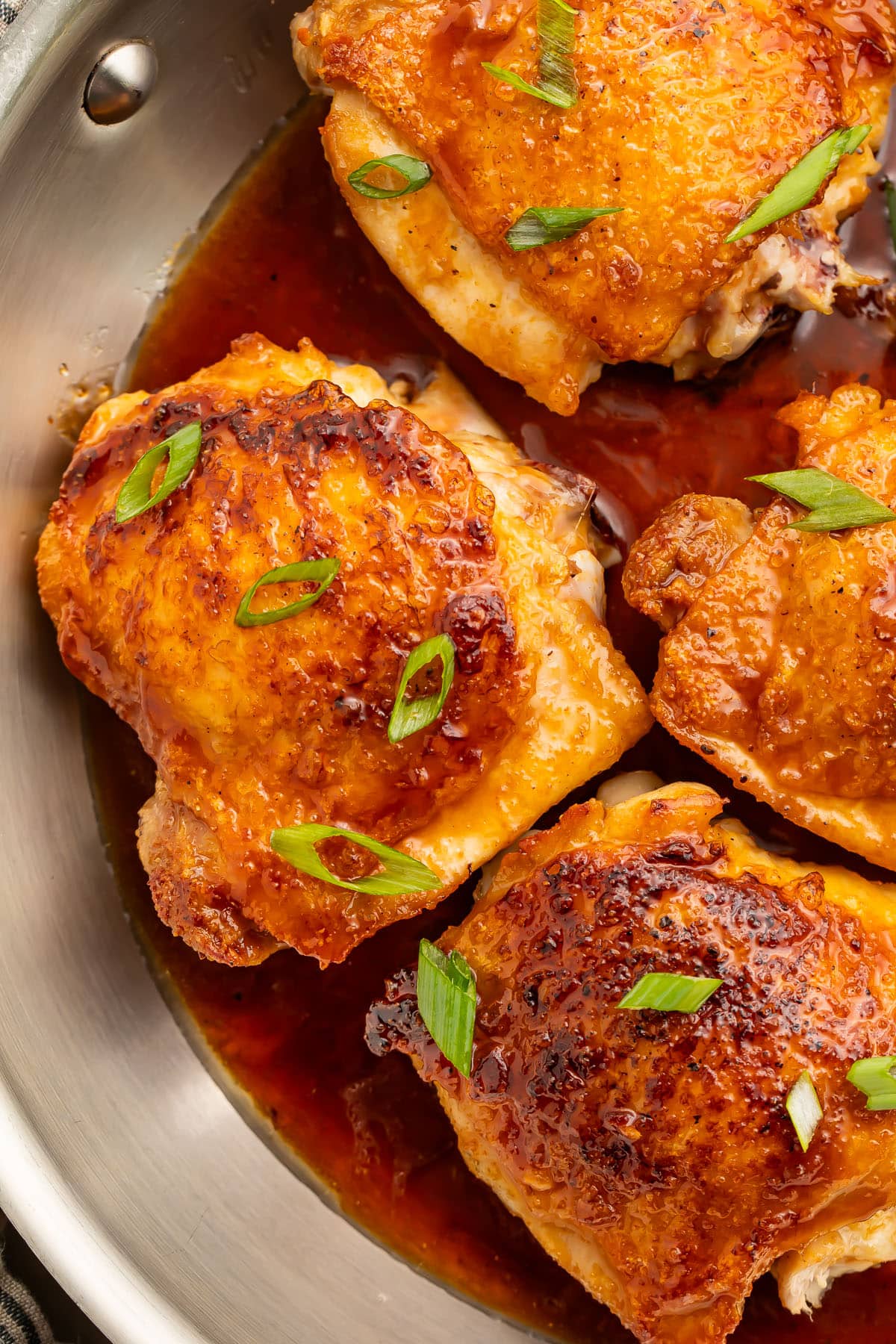 Close-up of Hot Honey Chicken being drizzled with glossy hot honey glaze over a cast iron skillet, with visible caramelization and fresh herb garnish