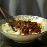 A beautifully plated bowl of Hungarian Goulash with tender beef chunks in a deep red paprika broth, garnished with fresh parsley and served alongside egg noodles, photographed on a rustic wooden table