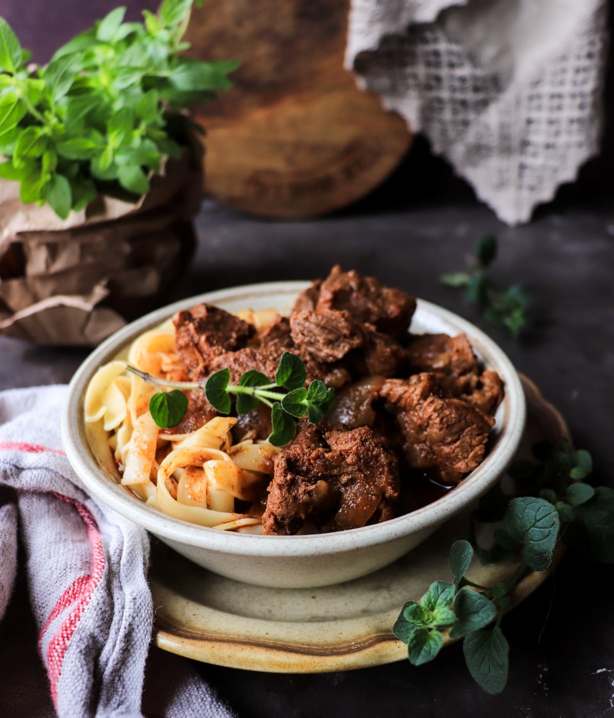 A beautifully plated bowl of Hungarian Goulash with tender beef chunks in a deep red paprika broth, garnished with fresh parsley and served alongside egg noodles, photographed on a rustic wooden table