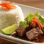 Indonesian Beef beautifully plated in a wide shallow bowl, garnished with fresh herbs, crispy shallots, and a wedge of lime on a warm wooden surface