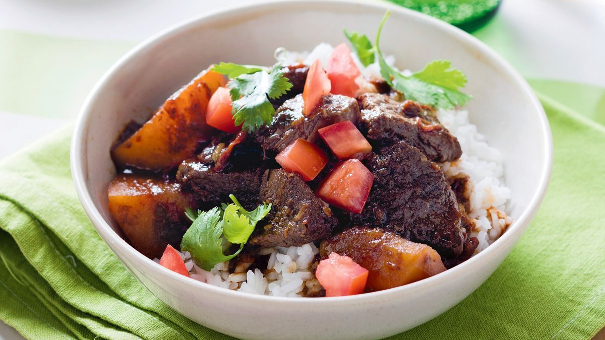 Close-up of Indonesian Beef in a bowl over steamed jasmine rice, sauce glistening, garnished with crispy fried shallots and a sprig of fresh cilantro