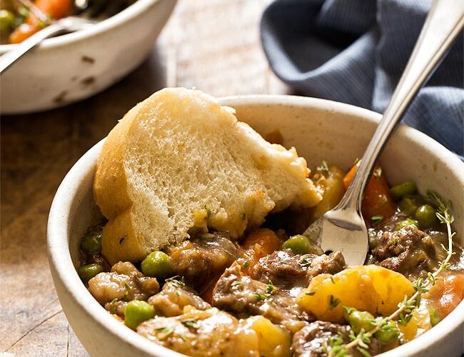 Instant Pot beef stew served in rustic ceramic bowls with fresh herbs and crusty bread, showing tender beef and colorful vegetables in rich broth