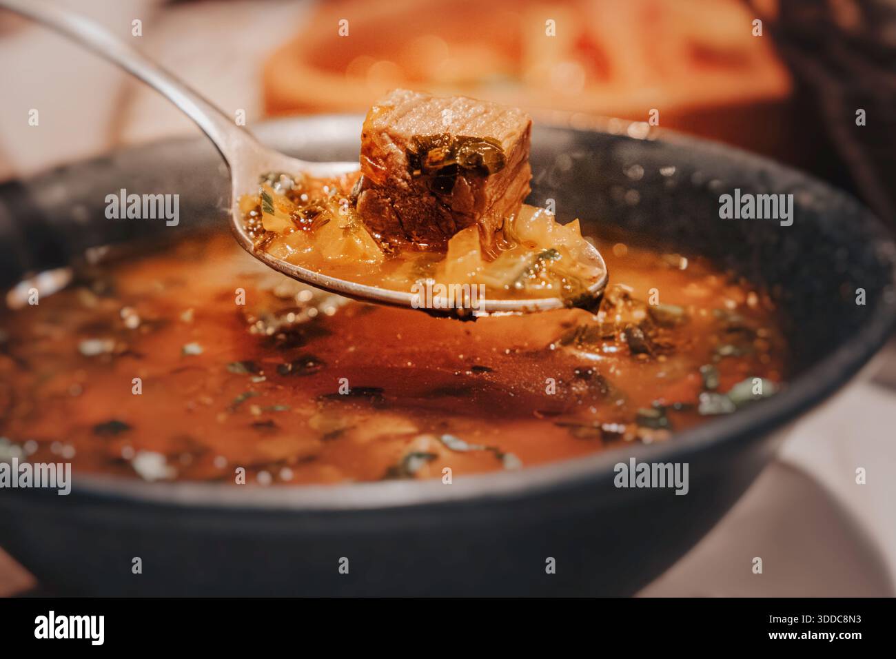 Close-up shot of a spoon lifting tender beef and vegetables from the stew, showing the rich, glossy broth and perfect texture