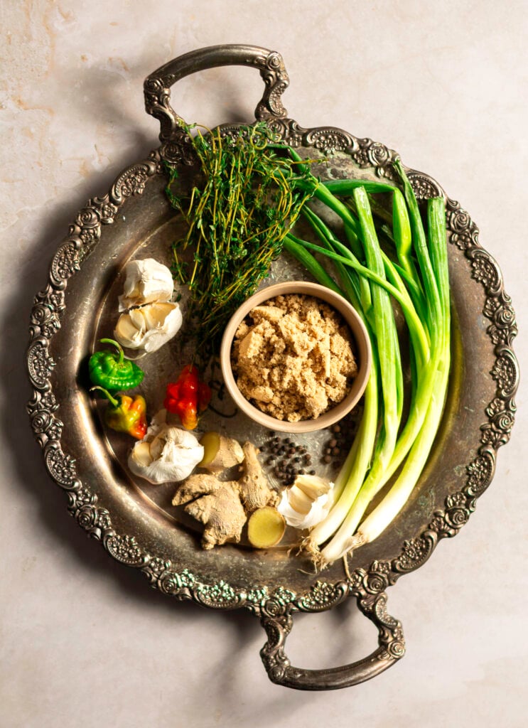 Jerk Chicken — Bold, Smoky, and Packed with Caribbean Flavor 27 Overhead flat-lay of jerk chicken marinade ingredients including scotch bonnet peppers, allspice berries, fresh thyme, green onions, ginger, garlic, and soy sauce arranged on a dark slate surface