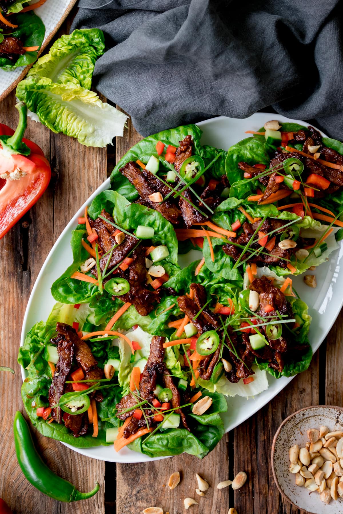 Overhead shot of healthy Korean BBQ lettuce wrap bowls styled on a wooden board with marinated grilled beef, crisp butter lettuce cups, shredded carrots, cucumbers, and sesame seeds, with small dipping sauce bowls on the side