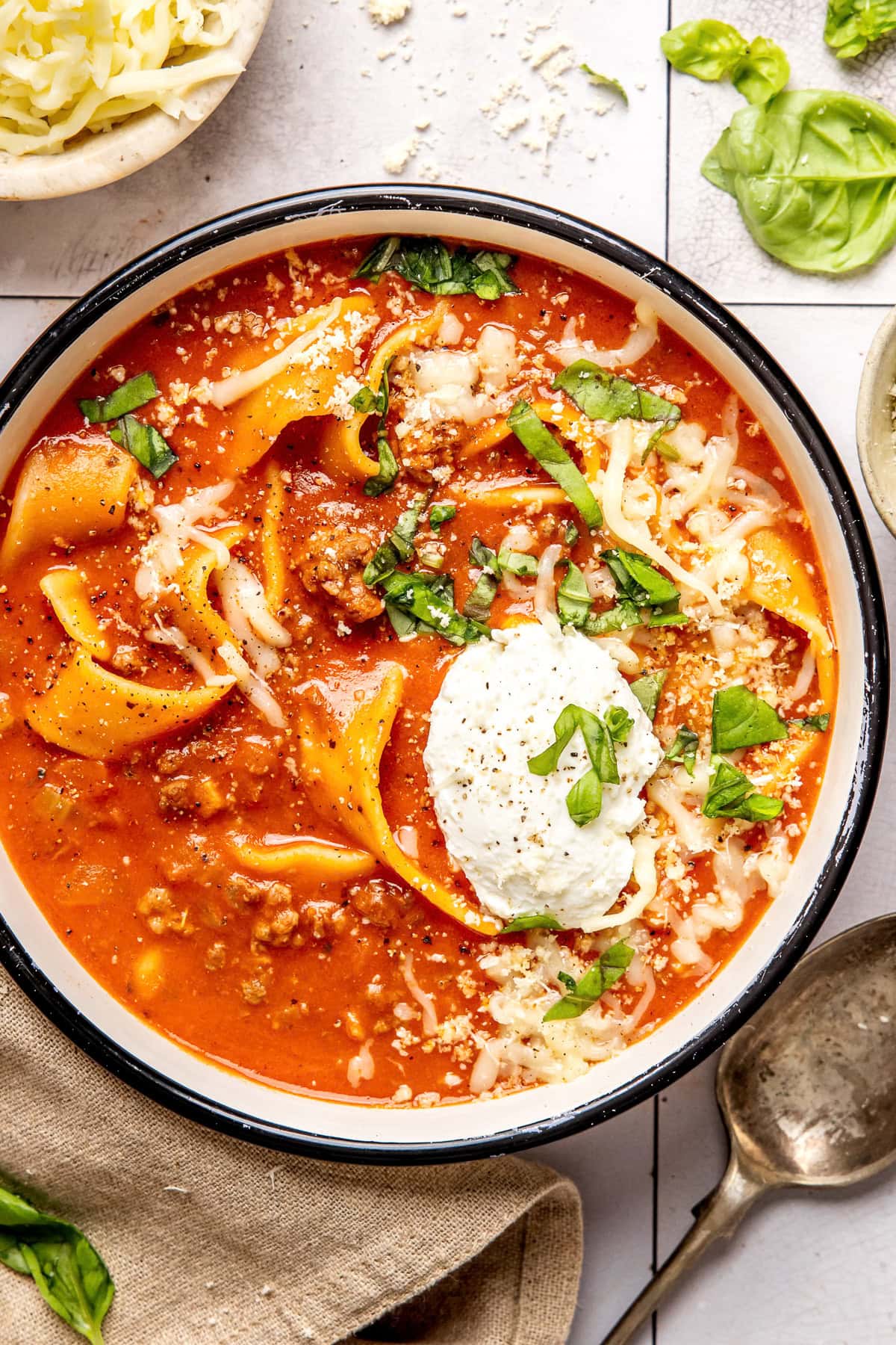 Lasagna Soup — All the Comfort of Lasagna in One Cozy Bowl 26 A rustic ceramic bowl filled with lasagna soup topped with a swirl of creamy ricotta, shredded mozzarella, and fresh basil, photographed in warm natural light on a dark wood surface