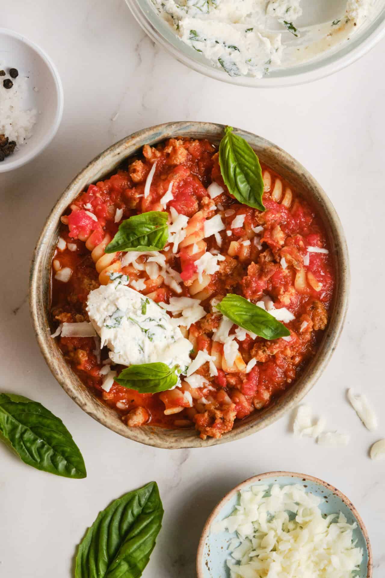 Lasagna Soup — All the Comfort of Lasagna in One Cozy Bowl 28 A close-up overhead shot of a bowl of lasagna soup with a generous spoonful of ricotta, fresh basil leaves, and a dusting of Parmesan, with crusty bread on the side and a linen napkin beneath the bowl