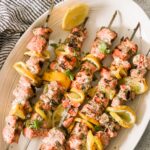 lemon garlic salmon skewers beautifully plated on a white serving board with lemon slices and fresh parsley garnish