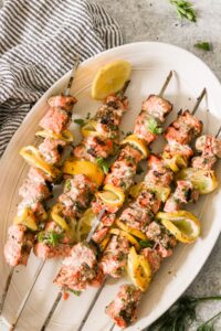 lemon garlic salmon skewers beautifully plated on a white serving board with lemon slices and fresh parsley garnish