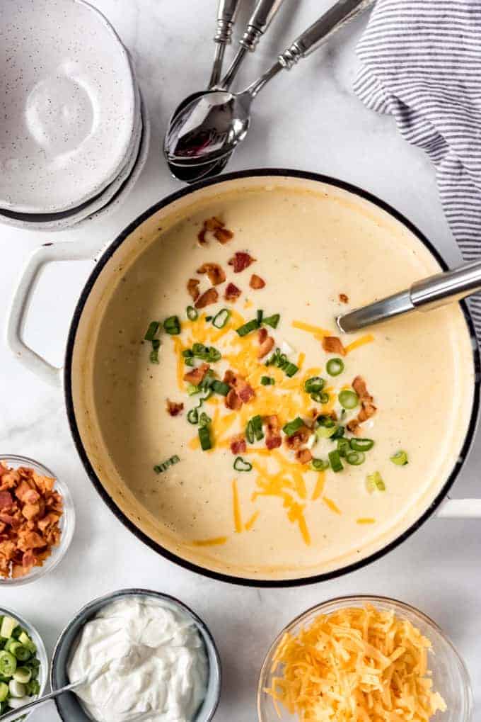 Loaded Baked Potato Soup — Creamy, Hearty & Worth Every Spoonful 28 A close-up overhead shot of a white ceramic bowl of loaded baked potato soup garnished with a generous pile of crispy bacon bits, melted shredded cheddar, a dollop of sour cream, and a scattering of bright green chives, steam rising gently from the bowl