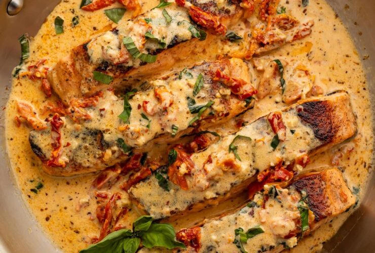 Marry Me Salmon fillets plated in a creamy sun-dried tomato cream sauce garnished with fresh basil and parmesan in a cast iron skillet
