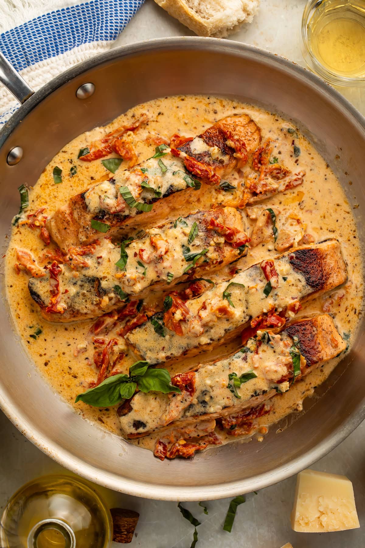 Marry Me Salmon fillets plated in a creamy sun-dried tomato cream sauce garnished with fresh basil and parmesan in a cast iron skillet