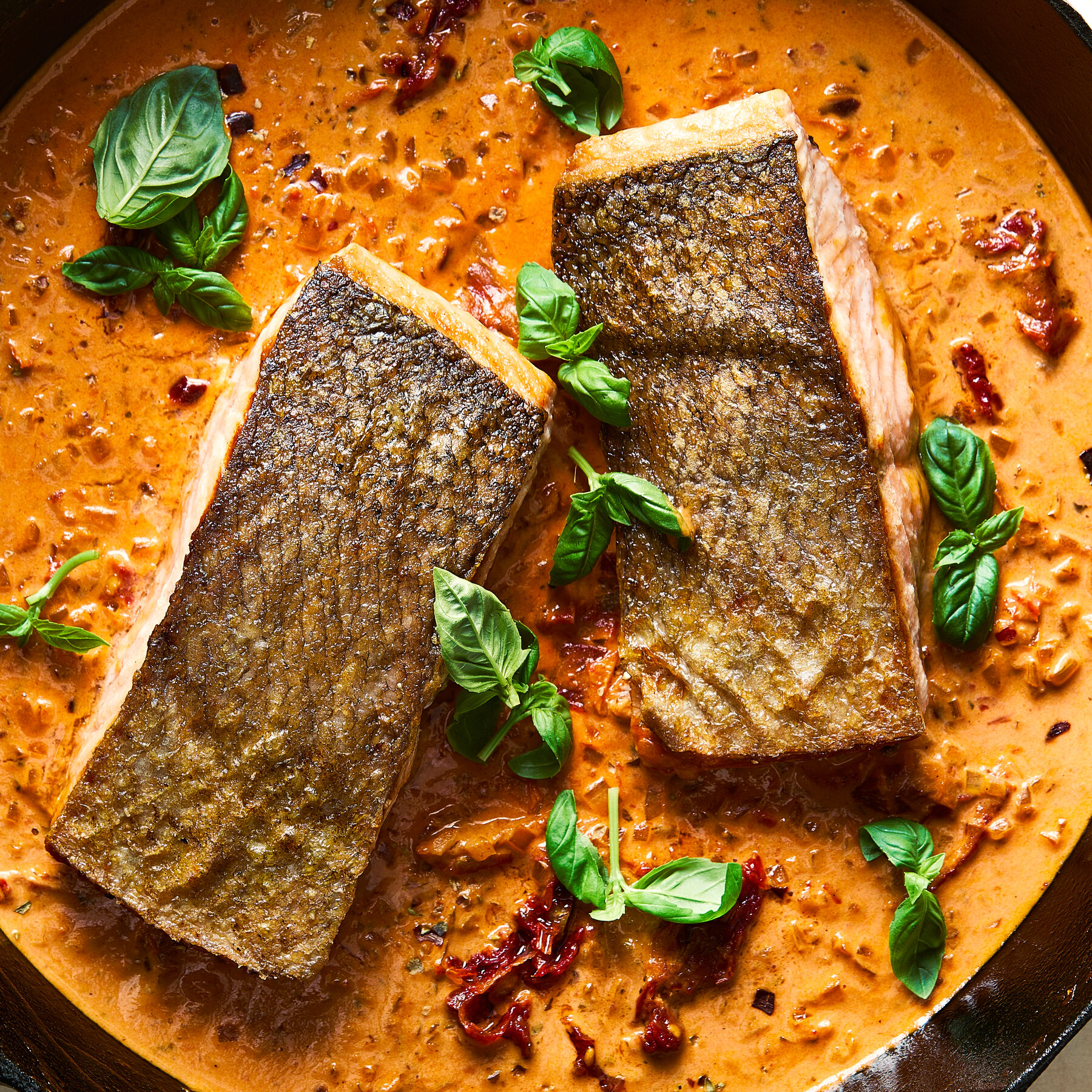 Ingredients for Marry Me Salmon laid out on a marble surface including salmon fillets, sun-dried tomatoes, garlic, cream, parmesan, and fresh herbs