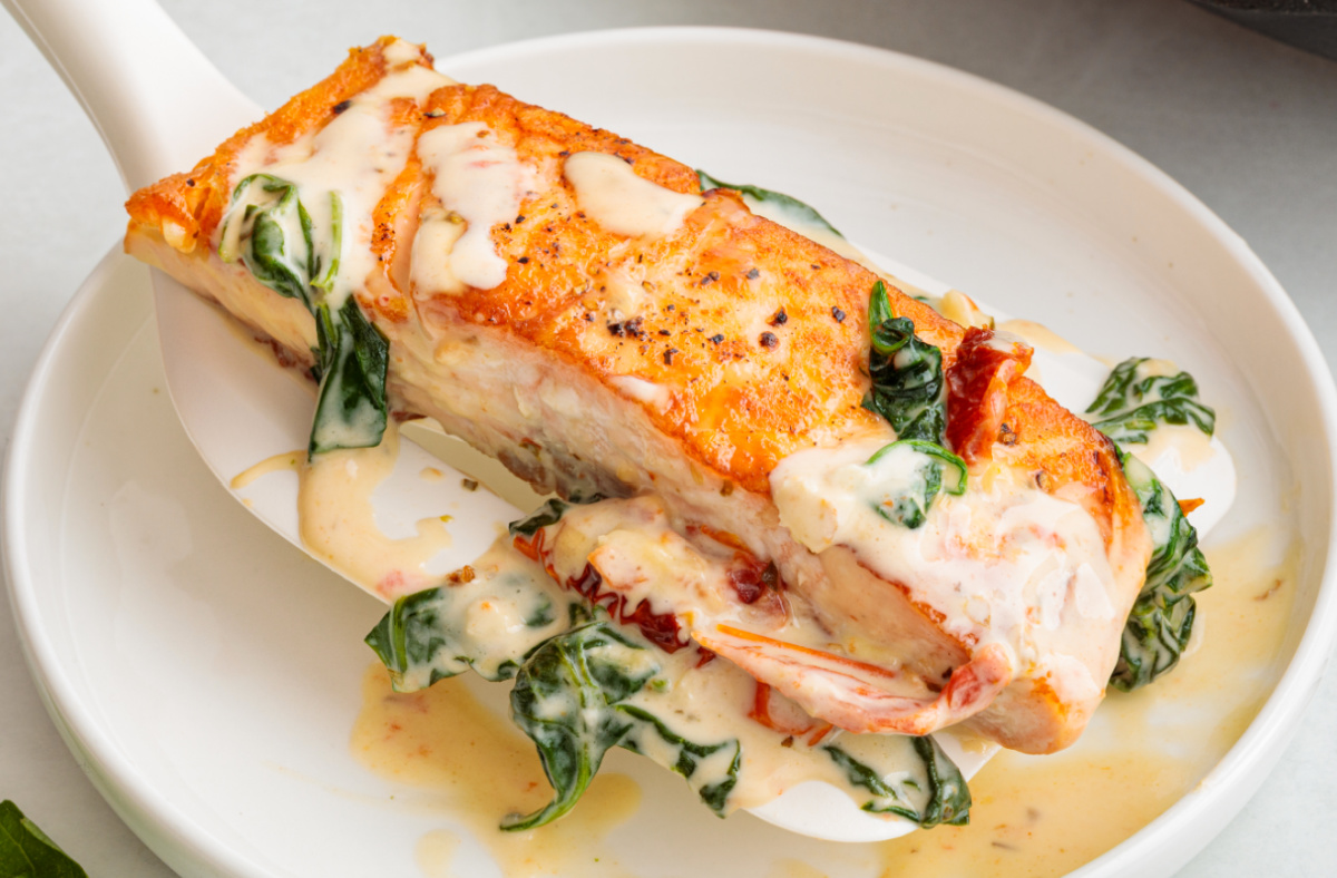 Close-up of Marry Me Salmon in a creamy sun-dried tomato sauce served over pasta with fresh basil leaves and grated parmesan on a white plate