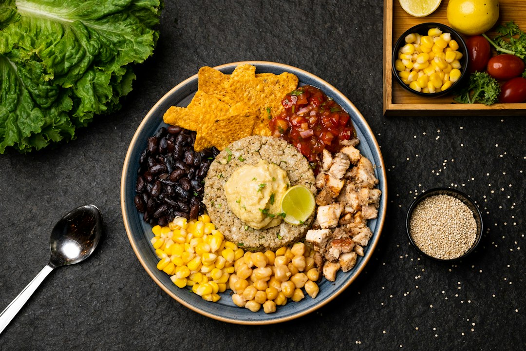Mexican street corn quinoa salad served in a wide white bowl, garnished with cotija cheese, fresh cilantro, chili powder, and lime wedges on a bright wooden surface