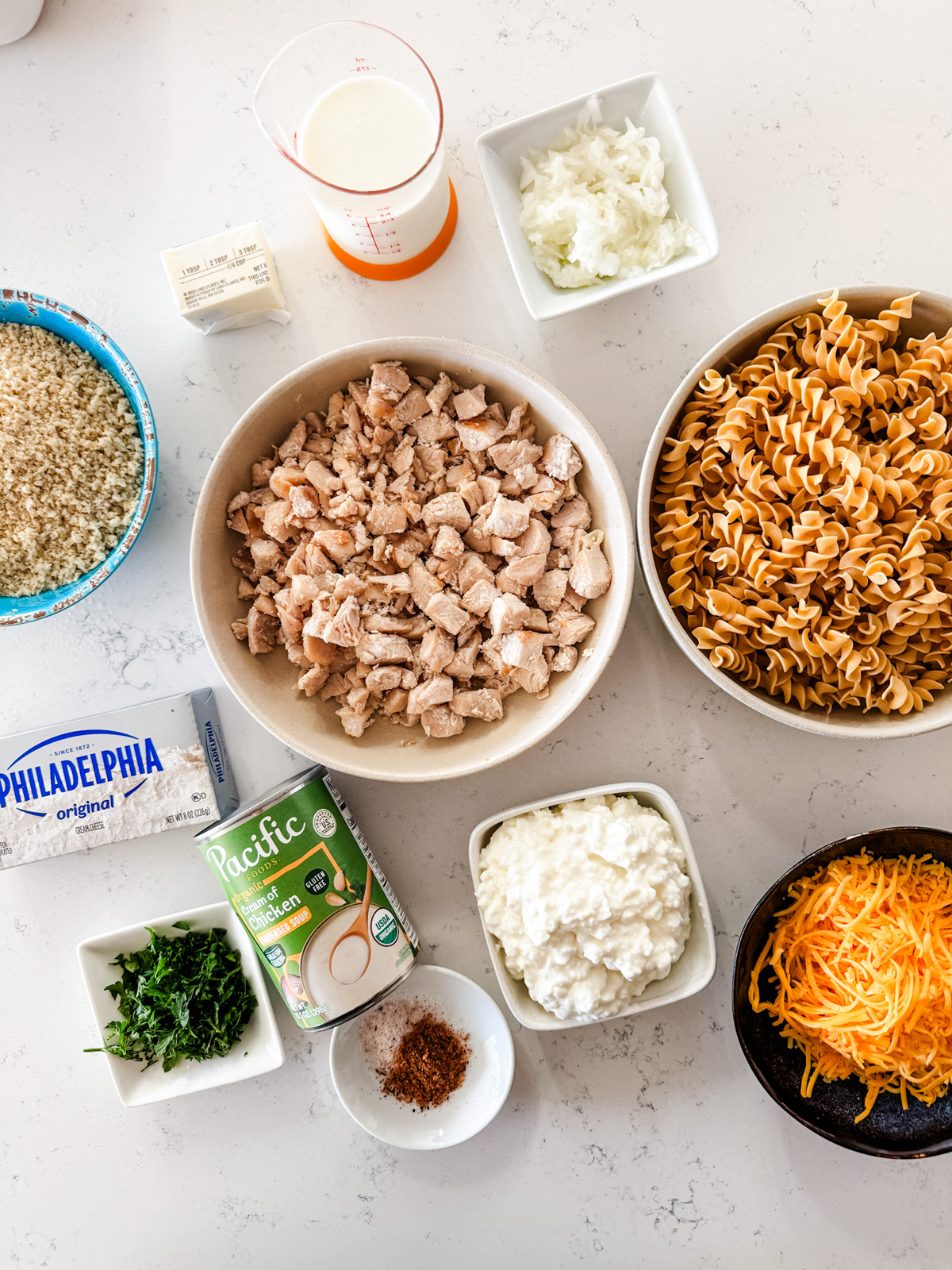 Overhead shot of million dollar chicken casserole ingredients — shredded rotisserie chicken, cream cheese, sour cream, crushed crackers, and butter arranged on a marble countertop