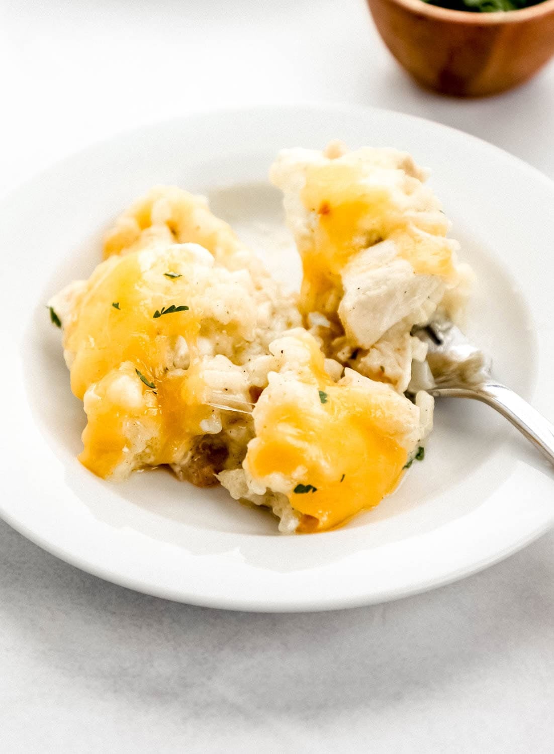 Close-up of a serving spoon lifting a portion of million dollar chicken casserole, showing the creamy filling and golden cracker topping, served on a white plate