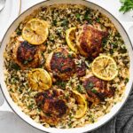 One Pan Chicken and Rice served in a cast iron skillet, garnished with fresh parsley and lemon wedges, golden chicken thighs resting on fluffy seasoned rice