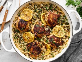 One Pan Chicken and Rice served in a cast iron skillet, garnished with fresh parsley and lemon wedges, golden chicken thighs resting on fluffy seasoned rice