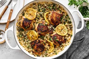 One Pan Chicken and Rice served in a cast iron skillet, garnished with fresh parsley and lemon wedges, golden chicken thighs resting on fluffy seasoned rice