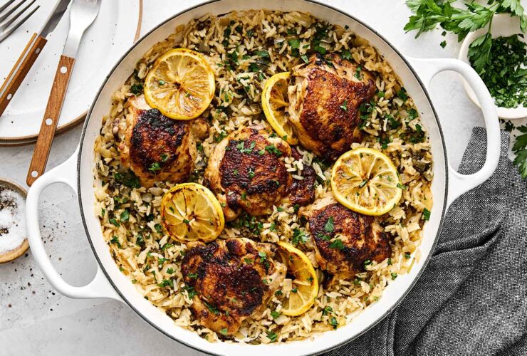 One Pan Chicken and Rice served in a cast iron skillet, garnished with fresh parsley and lemon wedges, golden chicken thighs resting on fluffy seasoned rice