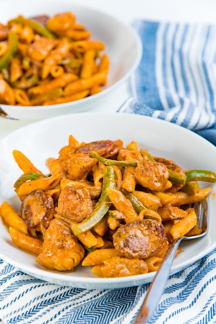 One Pot Creamy Cajun Chicken Pasta — Spicy, Smoky & Ready in 45 Minutes 27 Overhead flat-lay of raw ingredients for One Pot Creamy Cajun Chicken Pasta including sliced chicken breast, andouille sausage, colorful bell peppers, dry penne pasta, cream, spices, and fresh garlic on a wooden board
