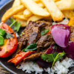 Peruvian Lomo Saltado plated beautifully in a wide bowl with golden french fries, tender beef strips, vibrant tomatoes and red onions, garnished with fresh cilantro