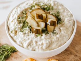 Pickle Dip — Creamy, Tangy, and Completely Addictive 36 creamy pickle dip in a white bowl garnished with fresh dill and chopped dill pickles, surrounded by crackers and vegetables on a wooden board